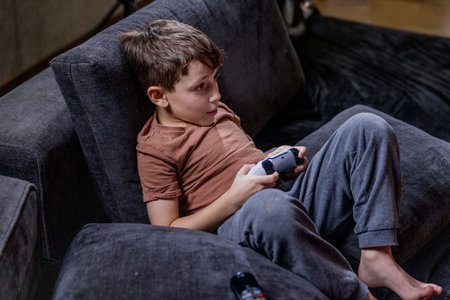 Boy is sitting on sofa at home and playing video games with his joypad