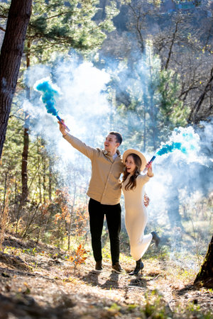Cheerful joyfully celebrating their pregnancy couple surrounded by blue smoke in a beautiful, lush forest.の写真素材