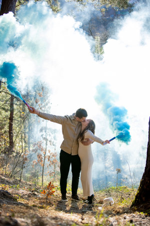 Cheerful joyfully celebrating their pregnancy couple surrounded by blue smoke in a beautiful, lush forest.の写真素材
