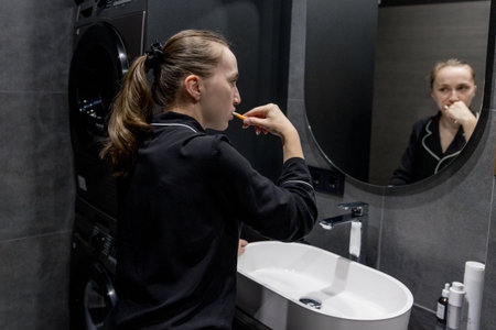 A woman in comfy pajamas brushes her teeth in a modern bathroom, enjoying her daily selfcare routine.の写真素材