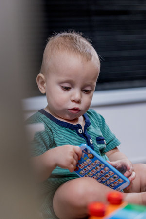 A small baby is happily sitting on the floor while engaging in play with a colorful toy phone, enjoying the experience of playtimeの写真素材