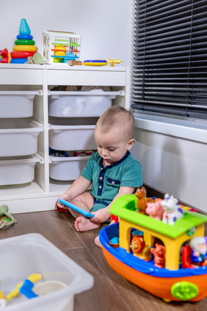 A small baby is comfortably sitting on the soft floor, joyfully playing with a variety of colorful toys scattered around himの写真素材