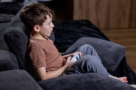 Boy is sitting on sofa at home and playing video games with his joypadの写真素材