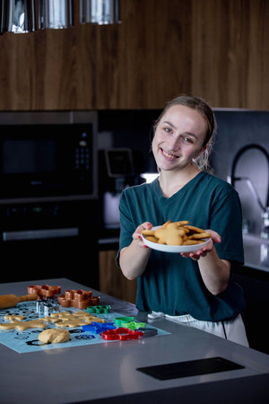 A joyful young girl is happily holding a plate full of freshly baked cookies in a modern kitchen setting.の写真素材