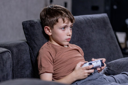 Boy is sitting on sofa at home and playing video games with his joypadの写真素材