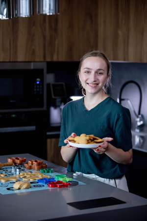 A joyful young girl is happily holding a plate full of freshly baked cookies in a modern kitchen setting.の写真素材