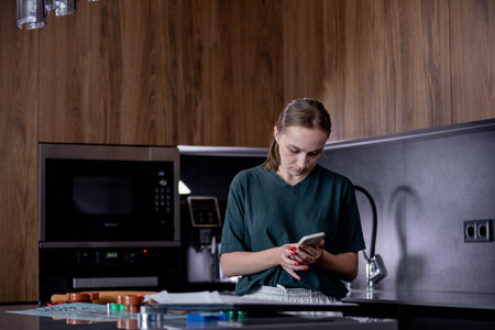 A person is seen using a modern smartphone while situated in an elegantly designed kitchen.の写真素材