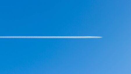 Plane in blue clear sky. White line in the middle of blue background.の写真素材