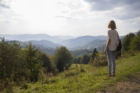 Girl on hiking trip enjoying the sunset view from above. Girl relax and refresh on mountain background is a landscape of high mountains, white clouds. Girl on the mountain looking at the sunny skyの写真素材