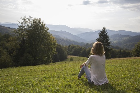 Girl on hiking trip enjoying the sunset view from above. Girl relax and refresh on mountain background is a landscape of high mountains, white clouds. Girl on the mountain looking at the sunny skyの写真素材