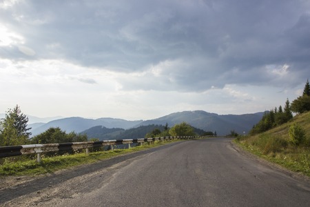 Curved serpentine mountain forest road in Ukrainian Carpathian. Asphalt highways and mountains under the blue sky. Empty asphalt road highway in the forested mountains, on the background a cloudy skyの写真素材