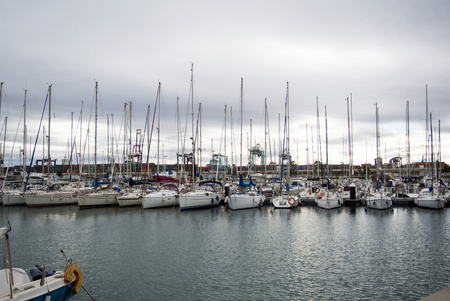 Luxury Yachts And Boats In Valencia Port At Mediterranean Sea. Reflexion in the water. White yachts are in the Spanish port of Valencia in the beginning of spring. Cloudy sky.の写真素材