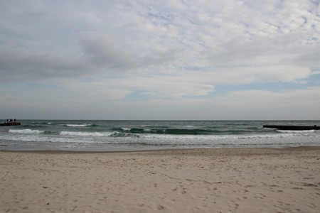 Cloudy weather. Golden sand, waves and foam. Cloudy day on the sandy beach. Panoramic view of beautiful sandy beach. Beach and waves with gloomy skyの写真素材