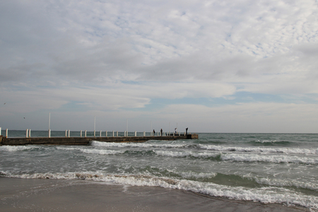 Cloudy weather. Golden sand, waves and foam. Cloudy day on the sandy beach. Panoramic view of beautiful sandy beach. Beach and waves with gloomy skyの写真素材