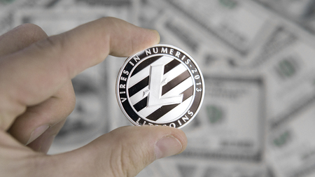 Litecoins crypto currency on US dollars in hand. Digital currency close-up. New virtual money. Real coins of Litecoins on banknotes of one hundred dollars. Bussiness, commercial.の写真素材