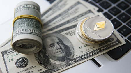 Ethereum cryptocurrency on top of 100 dollar biils on a laptop. Profit from mining crypto currencies. Miner with dollars and Ethereum money. BTC coin as symbol of electronic virtual money.の写真素材