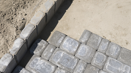 Process of fitting laying new exterior paving stones carefully placing one in position on a leveled and raked soil base. Sand foundation. Building.の写真素材