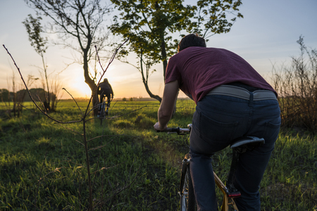 Man ride a bicycle in sunset. Riding a Bicycle at Sunset. Healthy Lifestyle Concept. Male ride bicycle in sun set. Biker ride a bike on sunsets sky on a field. Sport.の写真素材
