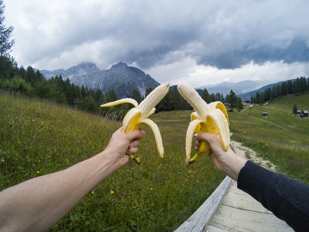 Tourists take a rest and eating babanas with a view on landscape of Dolomites moutains and a gree forest on a background. South Tyrol, Italy, Alp. Captured on action camera.の写真素材