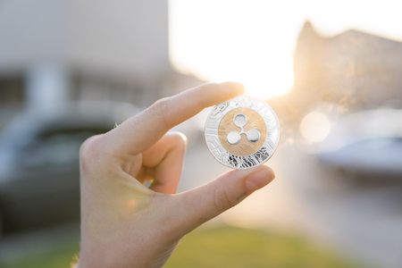 Golden silver Ripple coin in hand on a blurred sunset background. Hand holding a crypto currency virtual money. Bussiness, commercial, exchange, digital money.の写真素材