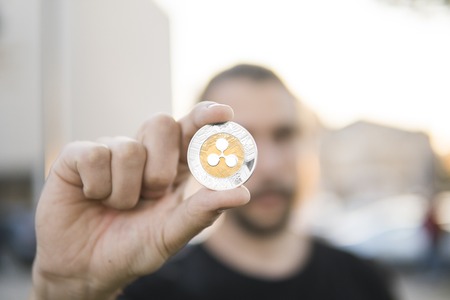 Golden silver Ripple coin in hand on a blurred sunset background with a man. Hand holding a crypto currency virtual money. Bussiness, commercial, exchange, digital money.の写真素材