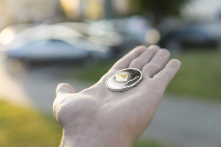 Golden silver Ethereum coin in hand on a blurred sunset background. Hand holding a crypto currency virtual money. Bussiness, commercial, exchange, digital money.の写真素材