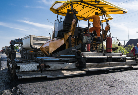 Worker operating asphalt paver machine during road construction and repairing works. A paver finisher, asphalt finisher or paving machine placing a layer of asphalt. Repavingの写真素材