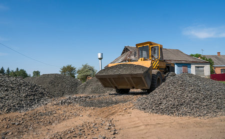 Yellow loader moving with uploaded bucket with stone gravel during road construction works. The...