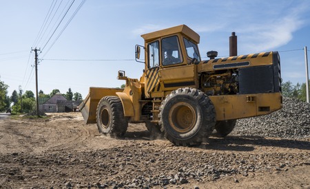 Yellow loader moving with uploaded bucket with stone gravel during road construction works. The stones for the road. Unloading stone.の写真素材