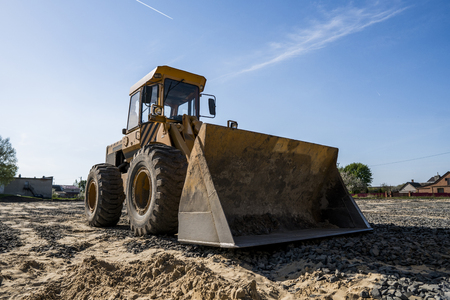 Yellow loader with empty bucket stands on a stone gravel during road construction works. The stones for the road. Unloading stone.の写真素材