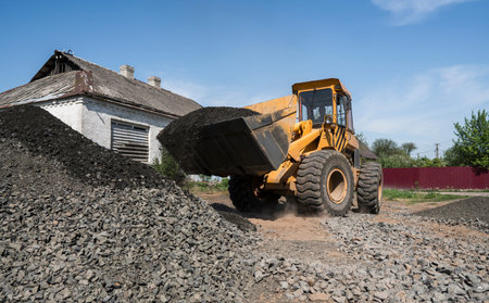 Yellow loader moving with uploaded bucket with stone gravel during road construction works. The...