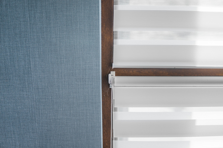 White fabric roller blinds on the plastic window with wood texture in the living room with blue wall.の写真素材