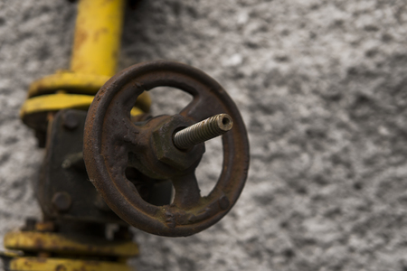 Old weathered gas crane and pipe on the background of a gray wall. Old gas gate of yellow colour is on a pipe and blocks a pipe. The pipeline with cranes for gas giving on the wall.の写真素材