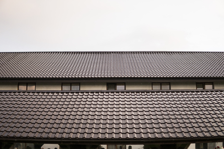 Modern roof covered with tile effect PVC coated brown metal roof sheets against cloudy sky.の写真素材