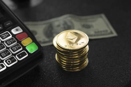 A pile of gold Ethereum coins and POS terminal with a hindred dollar banknote on a background. Ethereums Cryptocurrency. E-commerce, business, finance concept, banking and paymant.の写真素材