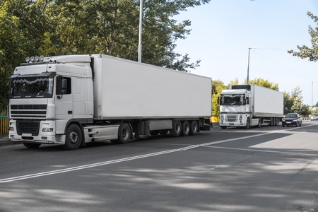 Two trucks on a road against blue sky and trees, cargo transportation concept.の写真素材