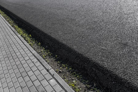 Close-up on a layer of new asphalt at the road under construction with a sidewalk road.の写真素材