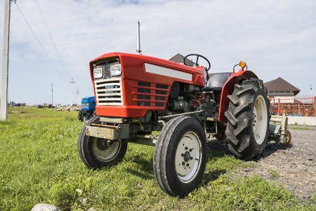 A small mini red tractor stands on a farm yard on green grass and waits for work to begin.の写真素材
