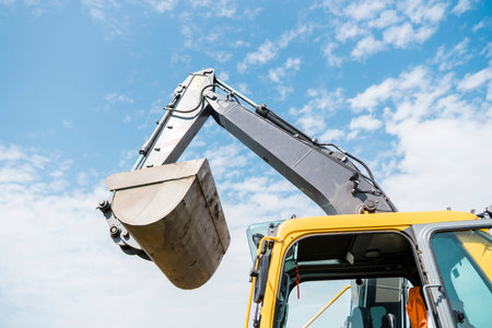 Bucket of yellow excavator loader standing against sunny cloudy sky during road construction and...