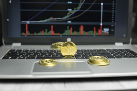 Golden Ethereum coin with gold coins lying around on a black keyboard of silver laptop and diagram chart graph on a screen as a background. Mining of ethereums online bussiness. Trading.の写真素材