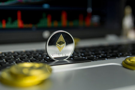 Golden Silver Ethereum coin with gold coins lying around on a black keyboard of silver laptop and...