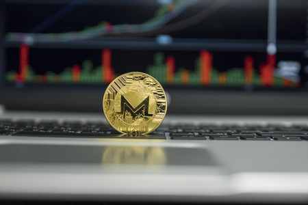 Golden coin of Monero on a black keyboard of silver laptop and diagram chart graph on a screen as a background. Cryptocurrency concept. Mining of ethereums online bussiness. Tradingの写真素材