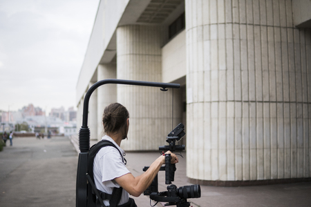 Professional videographer holding camera on 3-axis gimbal which mounted on easy rig. Videographer using steadicam. Pro equipment helps to make high quality video without shaking.の写真素材