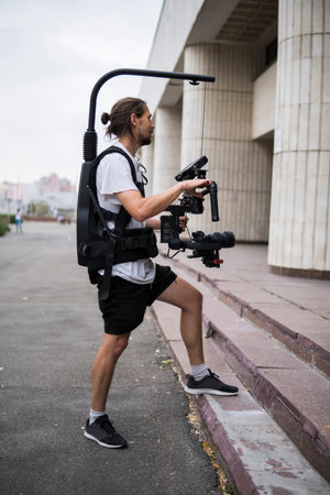 Professional videographer holding camera on 3-axis gimbal which mounted on easy rig. Videographer...