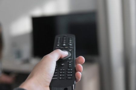 Hand holding remote control with television background in a living room.