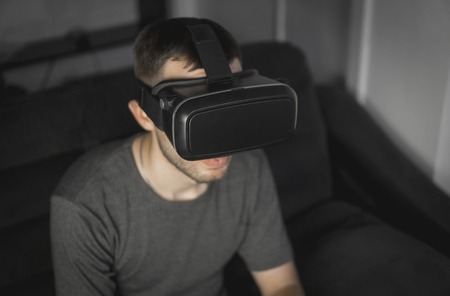 Young bearded man wearing headset of virtual reality in office sitting on a sofa.の写真素材
