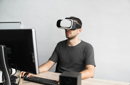 Young man wearing virtual reality goggles headset, vr box and sitting in the office against computer...