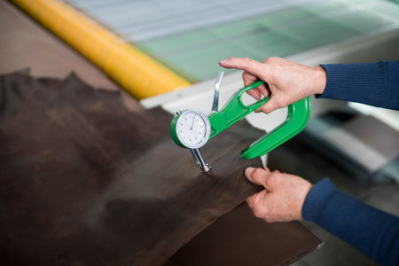 Woman hands use Leather thickness gauge on with a natural brown leather. Preparing of the raw...