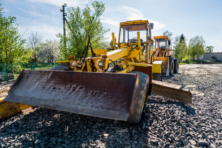 Yellow loader with empty bucket stands on a stone gravel during road construction works. The stones...