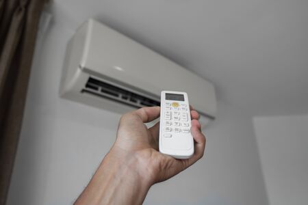 Mans hand using remote controler. Hand holding rc and adjusting temperature of air conditioner mounted on a white wall. Indooor comfort temperature. Health concepts and energy savings.の写真素材